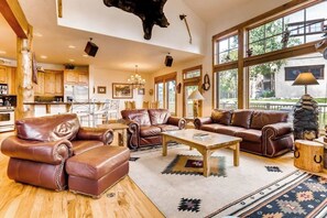 Ein geräumiges Wohnzimmer mit Ledersofas, einem Couchtisch und einem großen Fenster mit Blick ins Freie.
