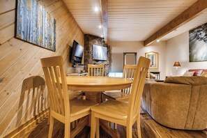 Ein Essbereich aus Holz mit einem runden Tisch, Stühlen, einer Steinsäule und einem Fernseher.