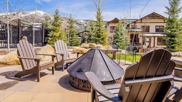 Een terras met Adirondack-stoelen, een vuurkorf en uitzicht op een berg.
