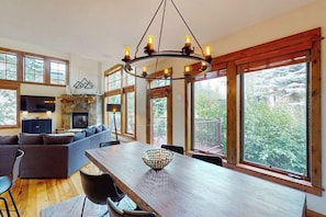 Ein modernes Interieur mit Essbereich, Kamin und großen Fenstern mit Blick ins Freie.