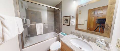 A modern bathroom with a glass-enclosed shower, a white toilet, a sink with a mirror, and a wooden vanity.