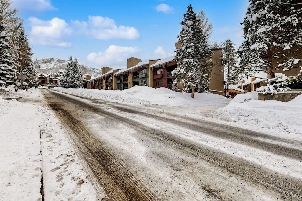 A snow-covered street with buildings on either side, including a multi-story structure with balconies.