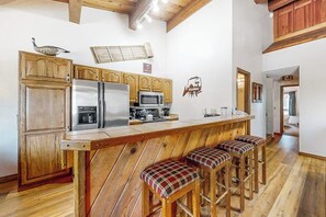 Eine Küche mit Holzausstattung, einem Edelstahlkühlschrank, einer Mikrowelle und einer Bar mit Karrostuhlen.