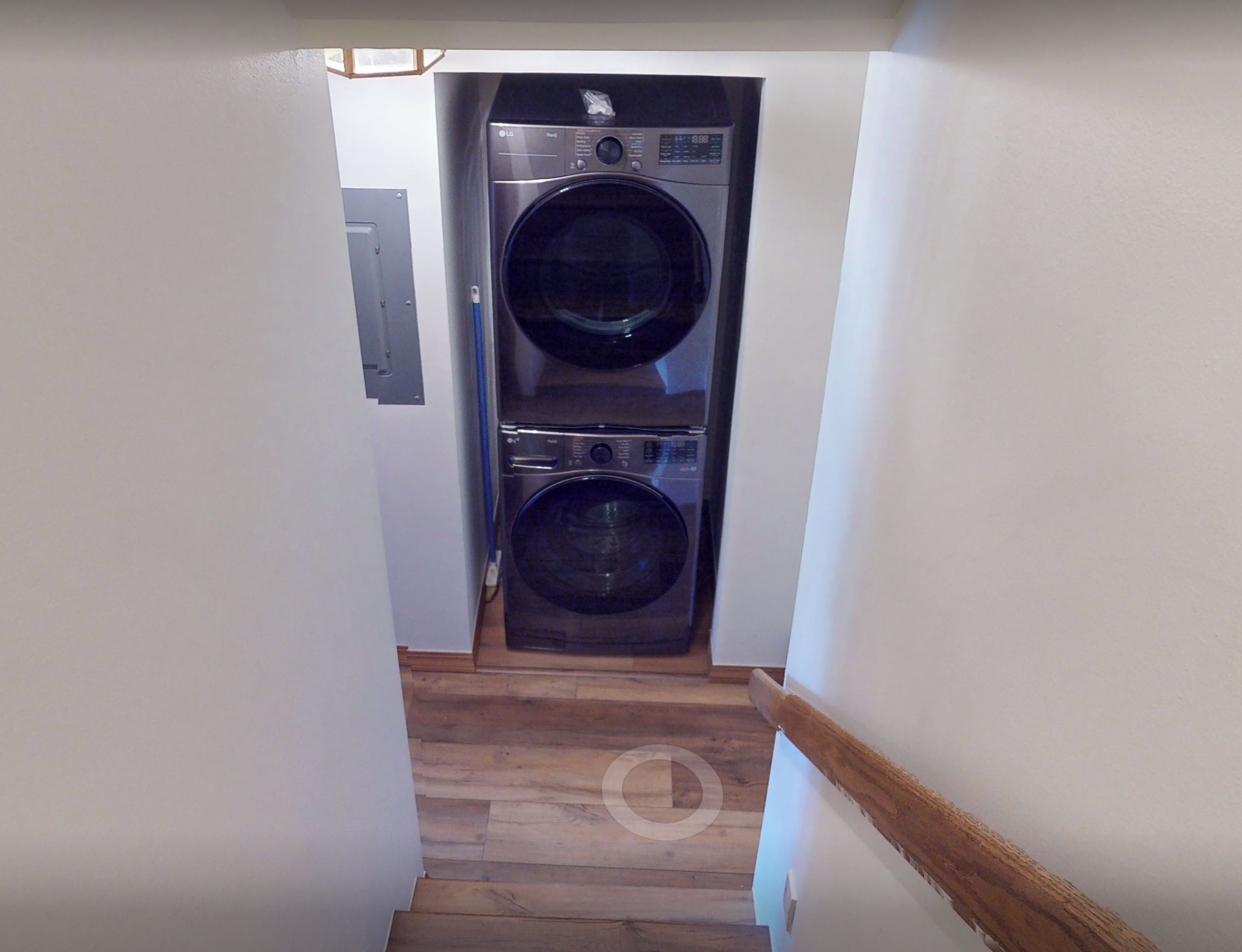 A laundry room with two stacked front-loading washing machines and a wooden staircase leading to another area.