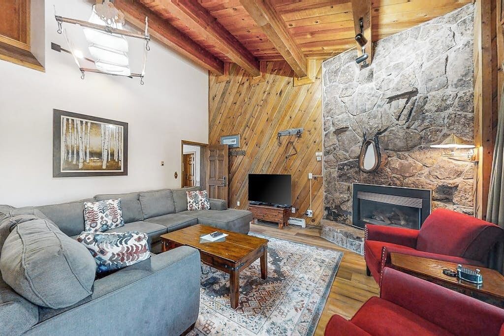 Una sala de estar con pared de piedra, vigas de madera en el techo, televisor y chimenea.