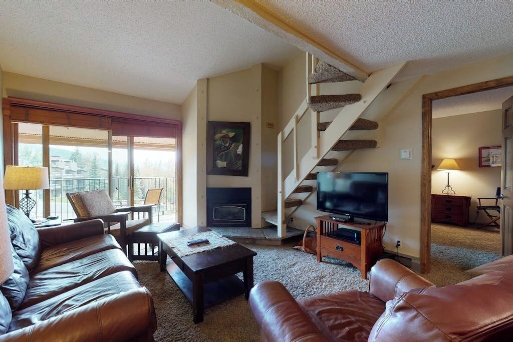Una sala de estar con chimenea, televisor, sofás de cuero, una escalera y un balcón con vistas.