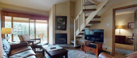 Una sala de estar con chimenea, televisor, sofás de cuero, una escalera y un balcón con vistas.