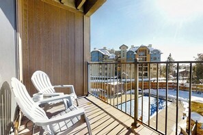 Ein Balkon mit weißen Stühlen und Blick auf ein Schwimmbecken und Gebäude.