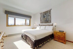 Ein Schlafzimmer mit einem Bett, einem Nachttisch, einer Lampe, einem Fenster und einem Wandbild.