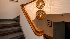 A staircase with wooden handrails, a woven pendant light, and a framed plant on the wall.