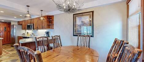 A spacious kitchen with wooden cabinets, a dining table, and chairs, a chandelier, and a framed picture on the wall.