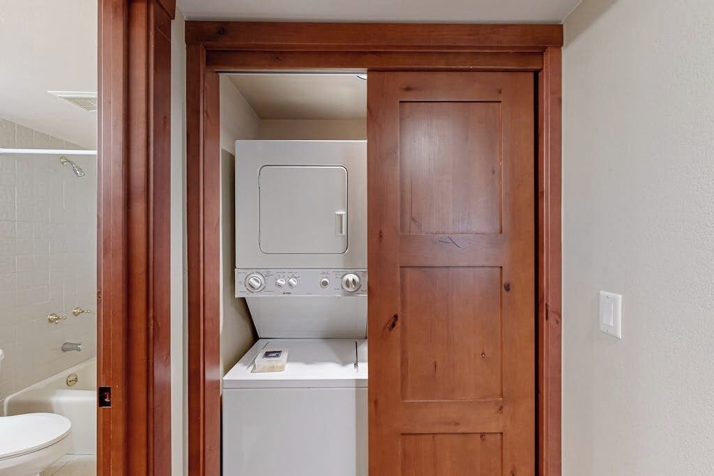 Une buanderie équip ée d’un lave-linge et d’un sèche-linge, avec une porte en bois et des toilettes blanches.