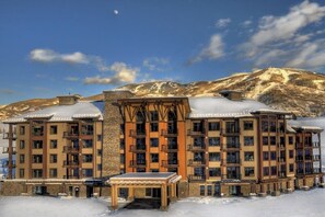 A multi-story hotel with balconies, a stone facade, and a snowy landscape in the background. - Brilliant upscale condo w/ADA accessibility & shared hot tubs, pool, gym, grills (Steamboat Springs)