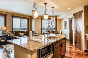 A kitchen with a large island, wooden cabinets, and pendant lighting. - Brilliant upscale condo w/ADA accessibility & shared hot tubs, pool, gym, grills (Steamboat Springs)