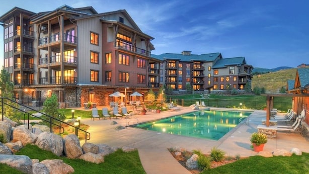 Un hotel de varios pisos con piscina, mobiliario exterior y jardines bien cuidados.