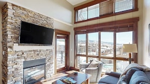 Una sala de estar con chimenea de piedra, televisor de pantalla plana, ventanas amplias y vistas a la ciudad.