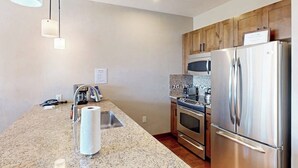 Una cocina con encimeras de granito, electrodomésticos de acero inoxidable, gabinetes de madera e iluminación colgante.