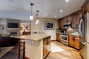 A modern kitchen with granite countertops, stainless steel appliances, wooden cabinets, and a stone backsplash. - Beautiful condo w/bonus den & shared pool, hot tubs, game room, fitness & more (Steamboat Springs)