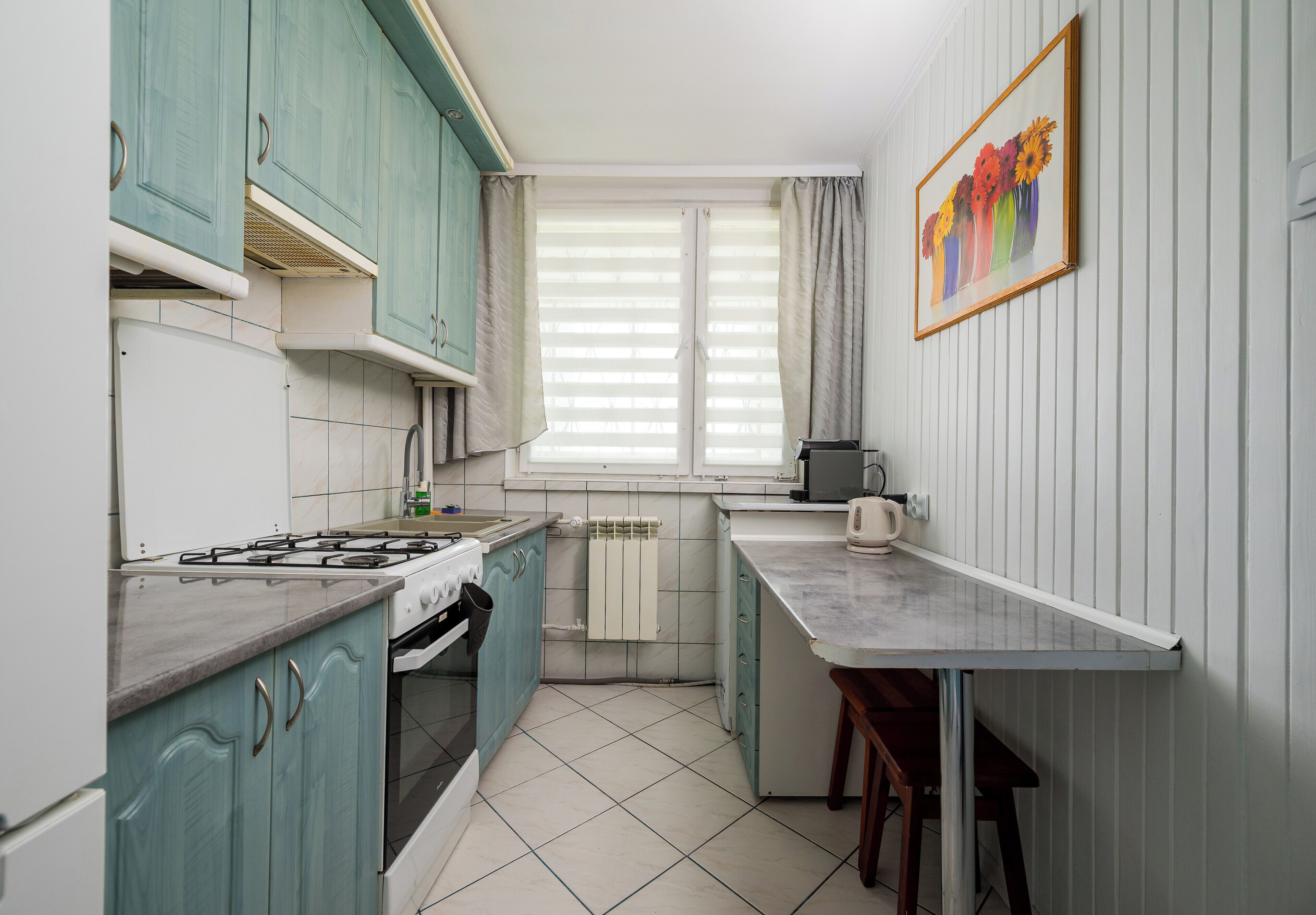 A kitchen with teal cabinets, a stove, a kettle, and a window with curtains.