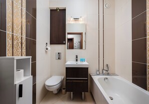 A bathroom with a toilet, sink, mirror, and bathtub. - Metro Trocka Charming Apartment (Warszawa)