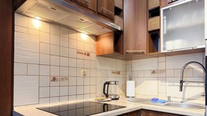 A modern kitchen with a black induction cooktop, wooden cabinets, and a stainless steel sink. - Rutkiewicz City Comfort Apartment (Wrocław)