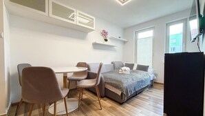 A modern room with a bed, a desk, and chairs. There are windows and a TV. - Rutkiewicz City Comfort Apartment (Wrocław)