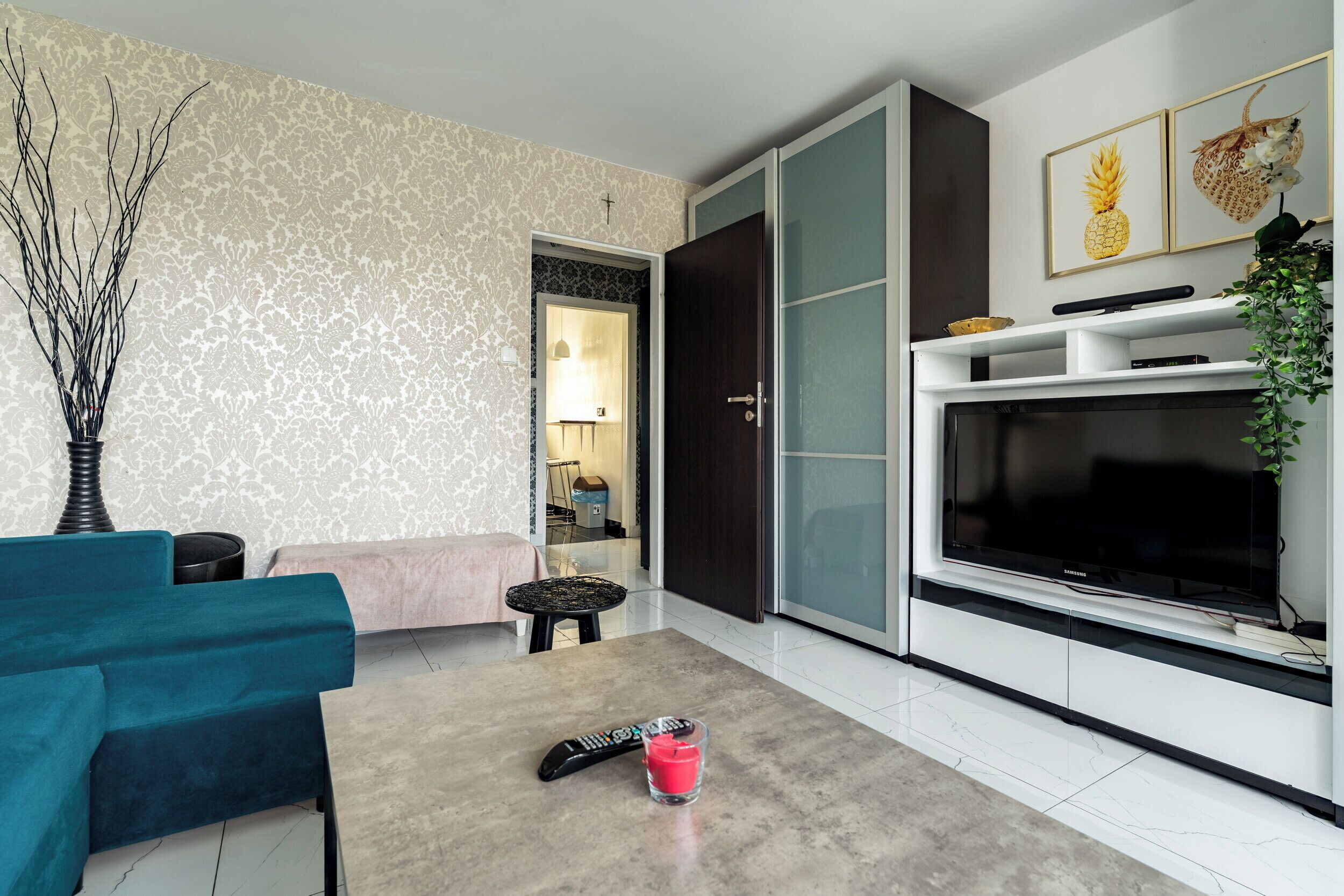 Uma sala de estar moderna com sofá, mesa de centro, televisão e porta para outro ambiente.