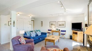 Una sala de estar con un sofá azul, un sillón púrpura, una mesa de centro de madera y un televisor.