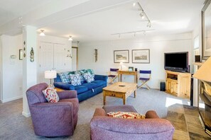 Ein Wohnzimmer mit einem blauen Sofa, einem violetten Sessel, einem Holztisch und einem Fernseher.