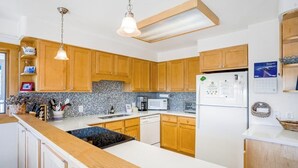 Una cocina con armarios de madera, encimera blanca, microondas, refrigerador y luces colgantes.