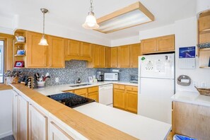 Eine Küche mit Holzausstattung, einer weißen Arbeitsplatte, einer Mikrowelle, einem Kühlschrank und hängenden Pendelleuchten.