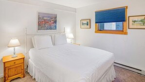 Un dormitorio con una cama, dos mesitas de noche, un ventanal con persianas y un cuadro en la pared.