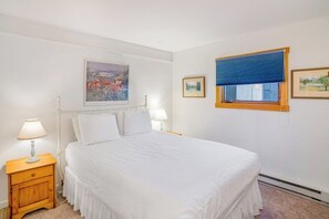 Ein Schlafzimmer mit einem Bett, zwei Nachttischen, einem Fenster mit Jalousien und Wandbildern.