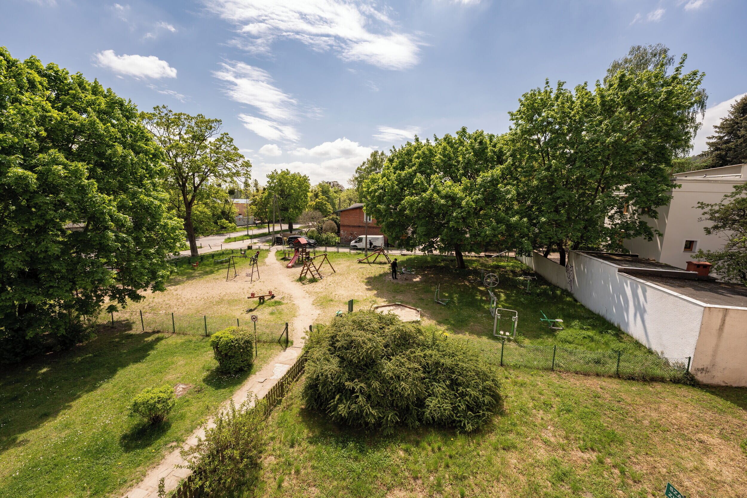 A park with playground equipment, a white building, and a clear sky.