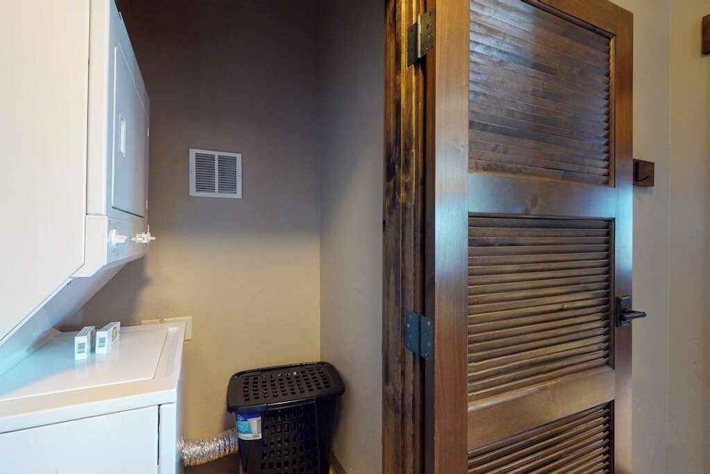 A laundry area with a washing machine, a dryer, a wooden door with a metal handle, and a black laundry basket.