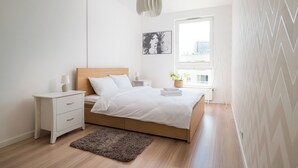A bedroom with a bed, bedside table, lamp, and a window with a view. - Kolska Chic Apartment (Warszawa)