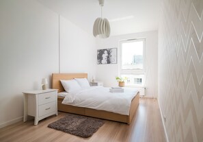 A bedroom with a bed, bedside table, lamp, and a window with a view. - Kolska Chic Apartment (Warszawa)