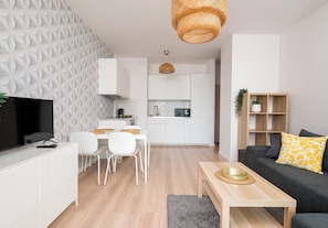 A modern living area with a dining table, sofa, TV, kitchen, and decorative wall. - Kolska Chic Apartment (Warszawa)