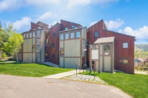 Ein modernes Mehrfamilienhaus mit Garagentor, einer kleinen Außenanlage mit Metallgeländer und blauem Himmel.