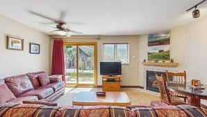 Una sala de estar con sofá, televisor, chimenea y ventilador de techo.