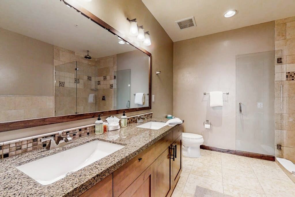 Une salle de bain avec deux lavabos, un grand miroir, une douche et des toilettes.