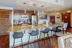 A modern kitchen with a central island, bar stools, and a dining area with a chandelier. - Deluxe condo next to Wildhorse gondola w/shared outdoor pool, hot tubs, gym (Steamboat Springs)