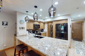 A kitchen with granite countertops, stainless steel appliances, wooden cabinets, and pendant lighting. - Top-floor, corner condo w/ mountain views plus a shared pool & gym (Steamboat Springs)