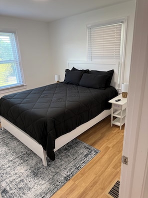 A bedroom with a bed, white nightstands, a bedside table, a window with blinds, and a door. - Spacious 3BR Home • Near Caesars Virginia • Ideal for Families & Work Stays (Danville)