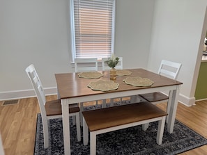 A dining table with four chairs, a bench, a vase with flowers, and a window with blinds. - Spacious 3BR Home • Near Caesars Virginia • Ideal for Families & Work Stays (Danville)