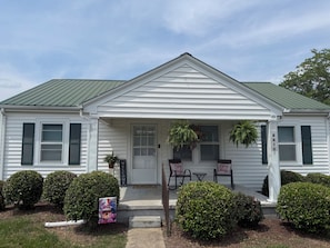 A white house with a green roof, a front porch with two chairs, and a welcome sign. - Spacious 3BR Home • Near Caesars Virginia • Ideal for Families & Work Stays (Danville)