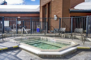 Ein 90 Zentimeter tiefes Whirlpool-Becken, umgeben von einem Metallzaun, mit Außenmöbeln und einem Gebäude im Hintergrund.