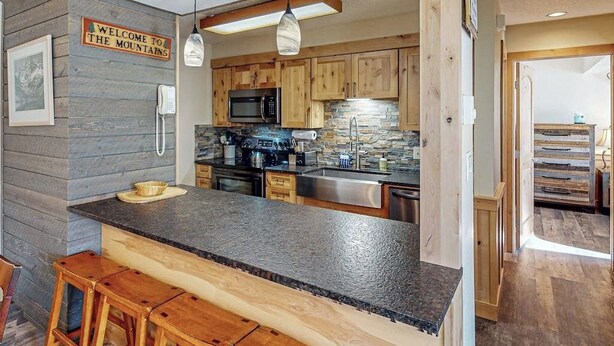 A kitchen with wooden cabinets, a granite countertop, a built-in oven, a microwave, and a stone backsplash. - Deluxe condo with private patio, pool & hot tub (Steamboat Springs)