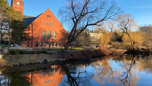 A red brick building with a clock tower, a pond reflecting the structure, and leafless trees. - Private Suite with Full Bath & Separate Entrance –  close to Tufts University (Winchester)
