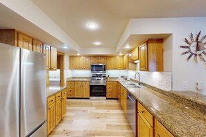 Eine moderne Küche mit Holzschränken, Edelstahlgeräten, Granit Arbeitsplatten und Einbaustrahler.